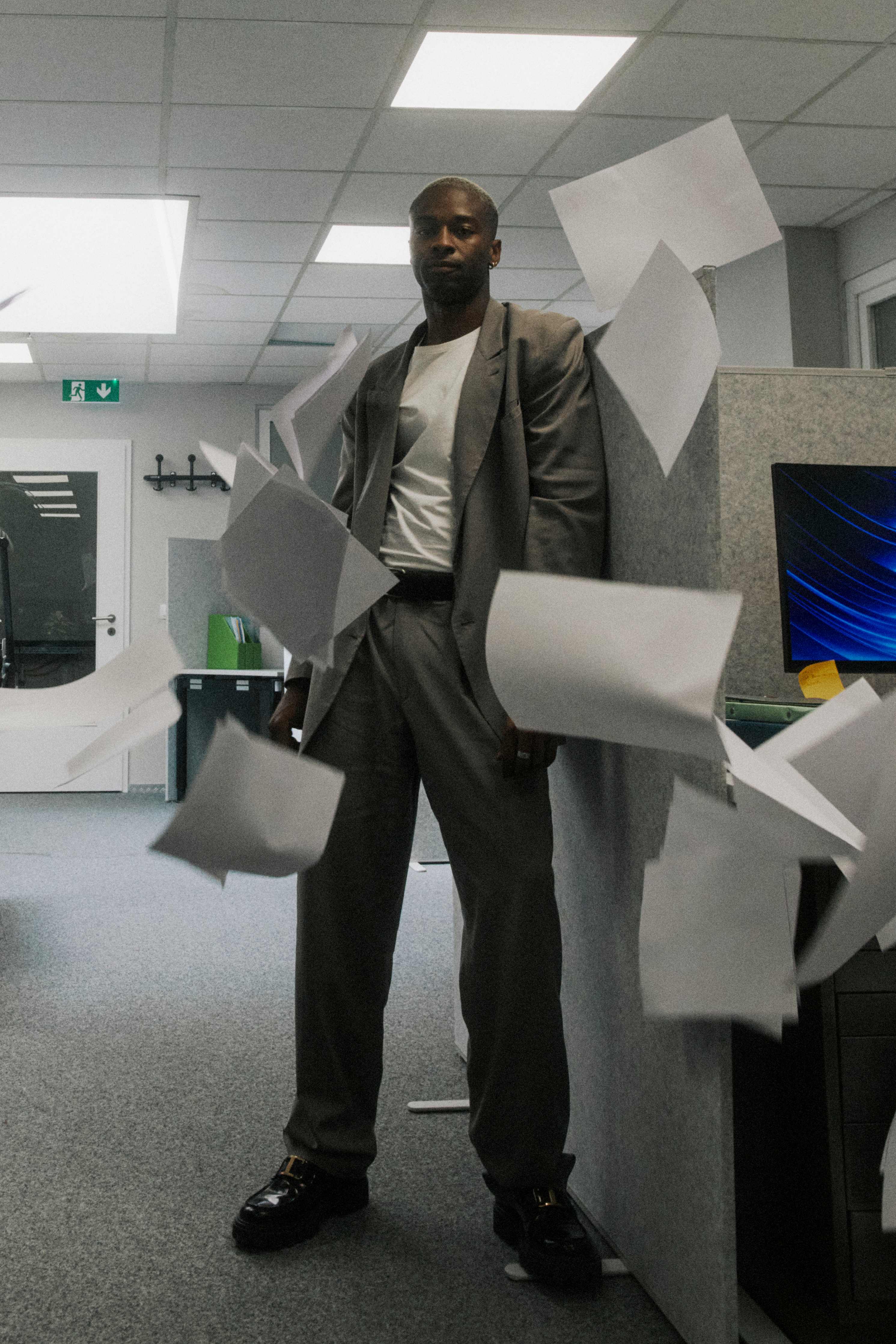 Man in a grey suit standing composed amid flying papers, full-length — The Ad Spend brand image