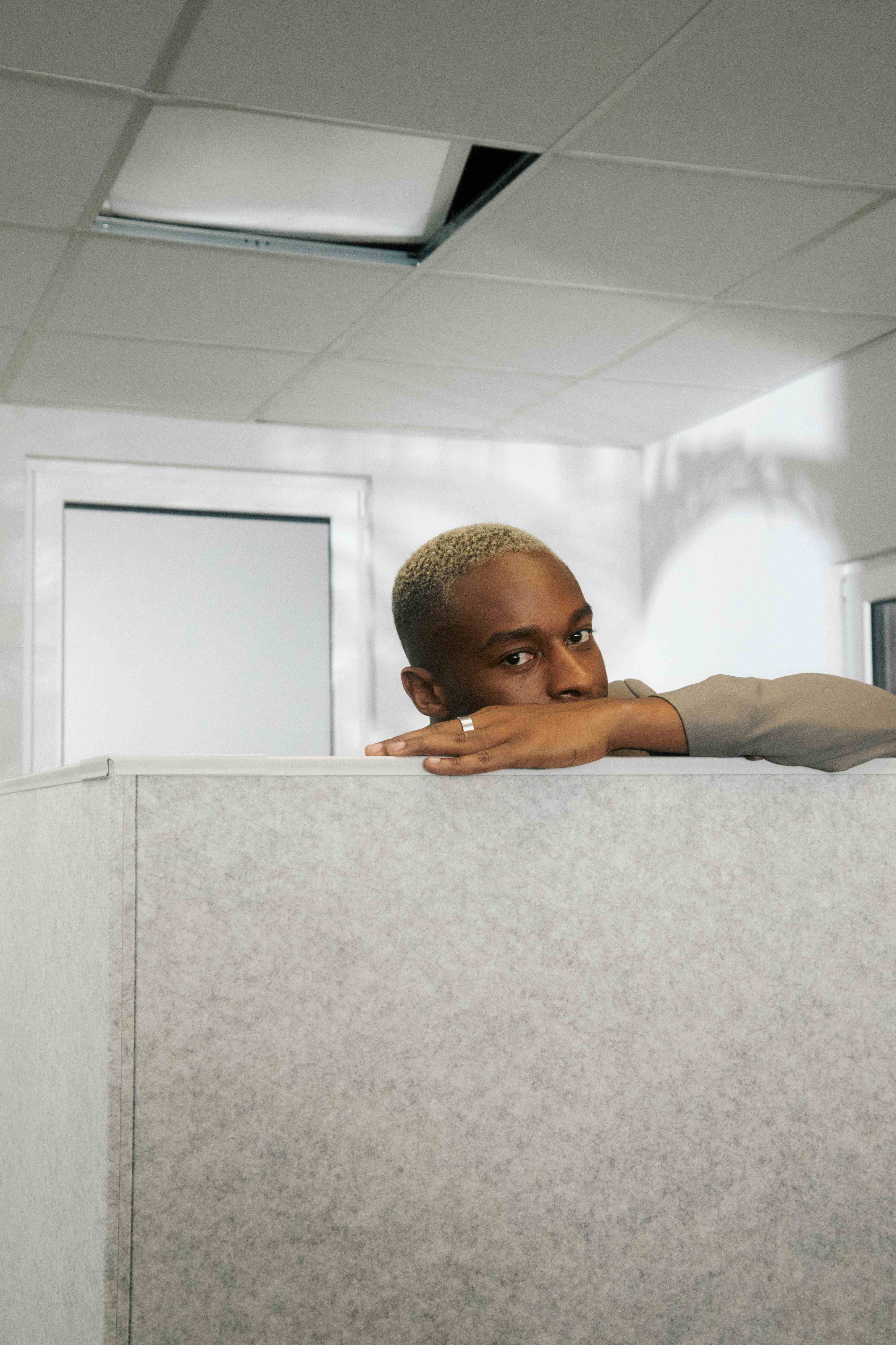 A man resting his head and arm on top of a grey cubicle partition, pensive — The Ad Spend brand image