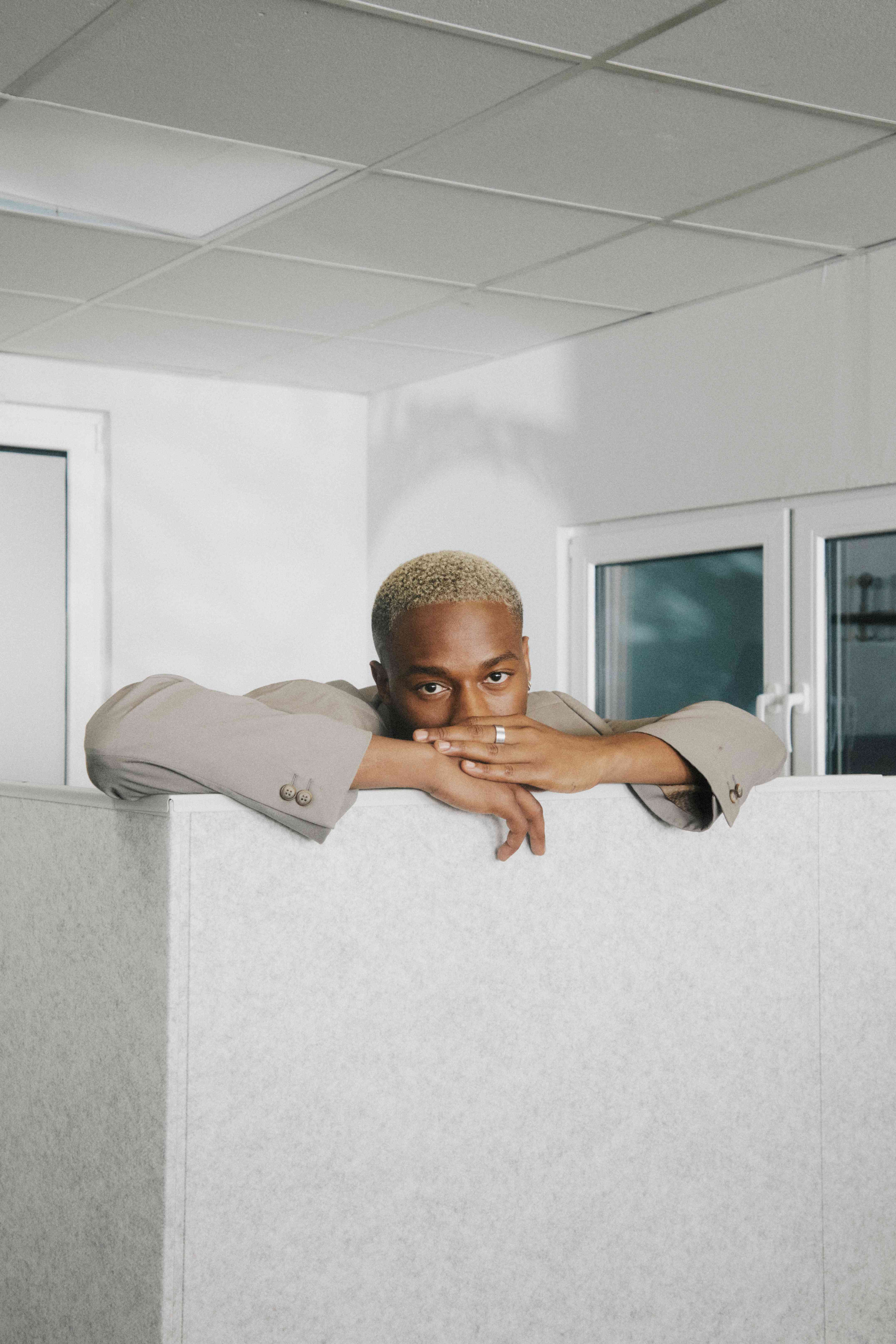 A person resting their chin on folded arms atop a cubicle wall, direct gaze — The Ad Spend brand image