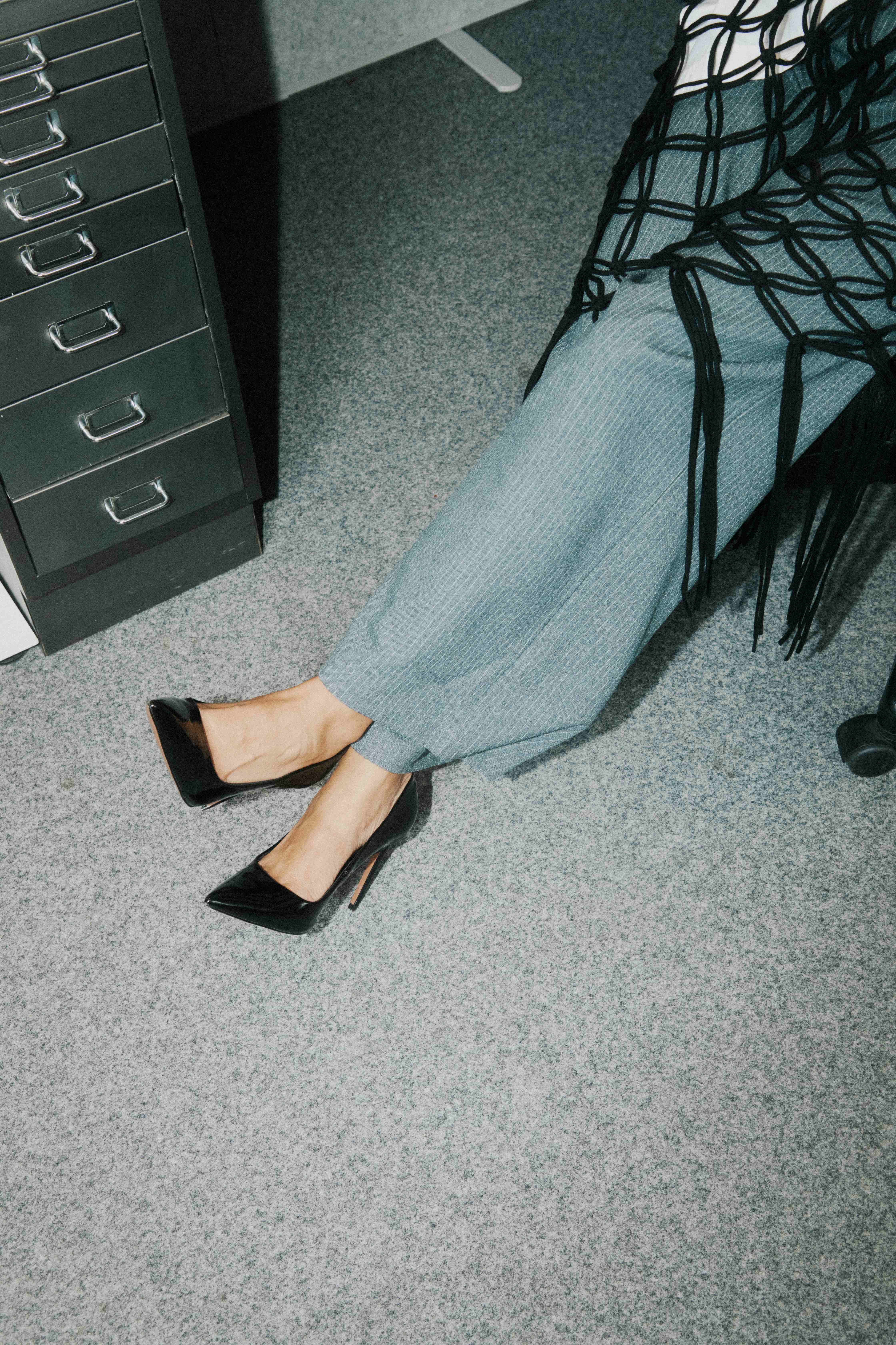 Overhead of black heels on grey carpet beside a filing cabinet — The Ad Spend brand image