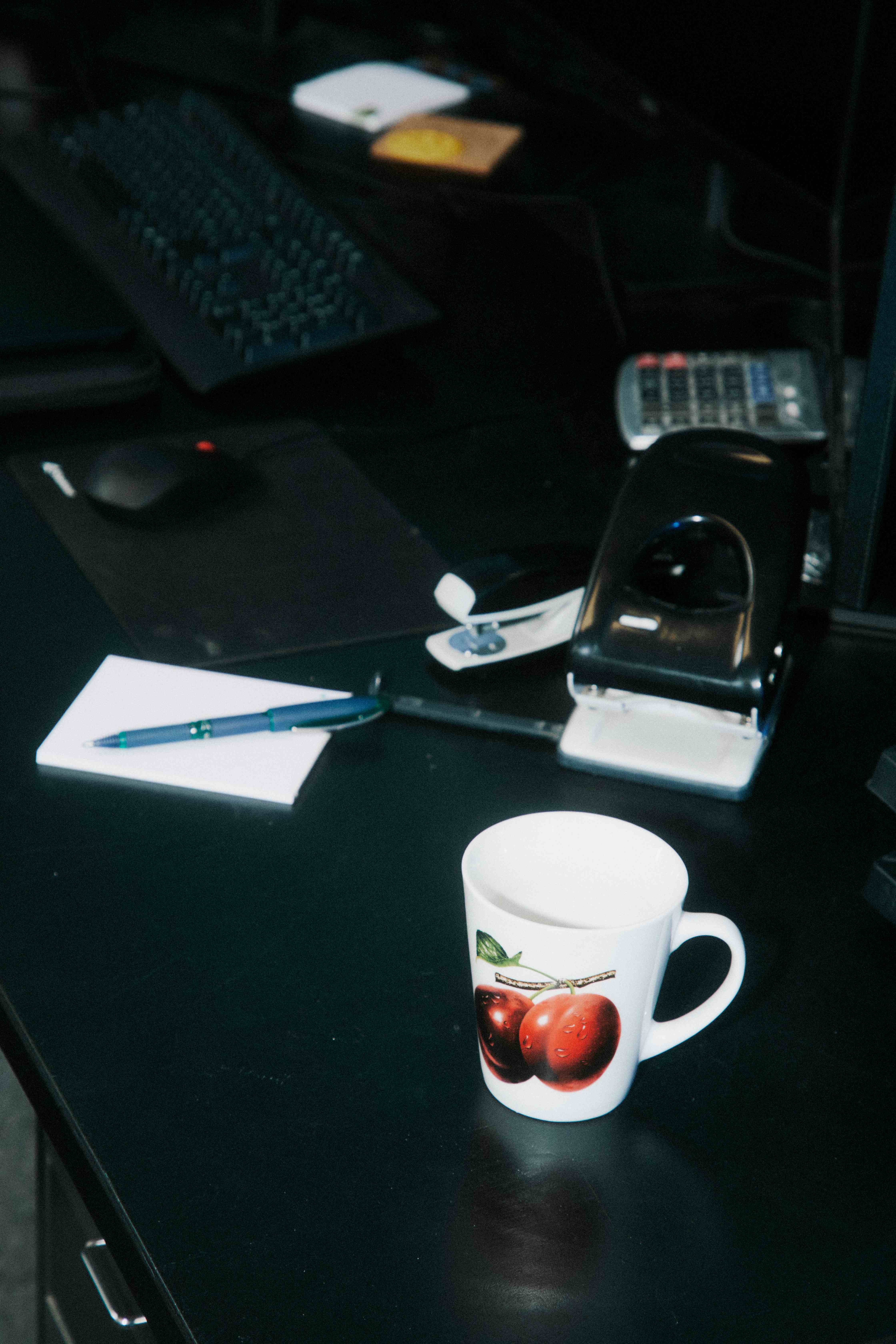 Moody dark desk with a cherry-print mug, notepad, pen, and hole-punch — The Ad Spend brand image