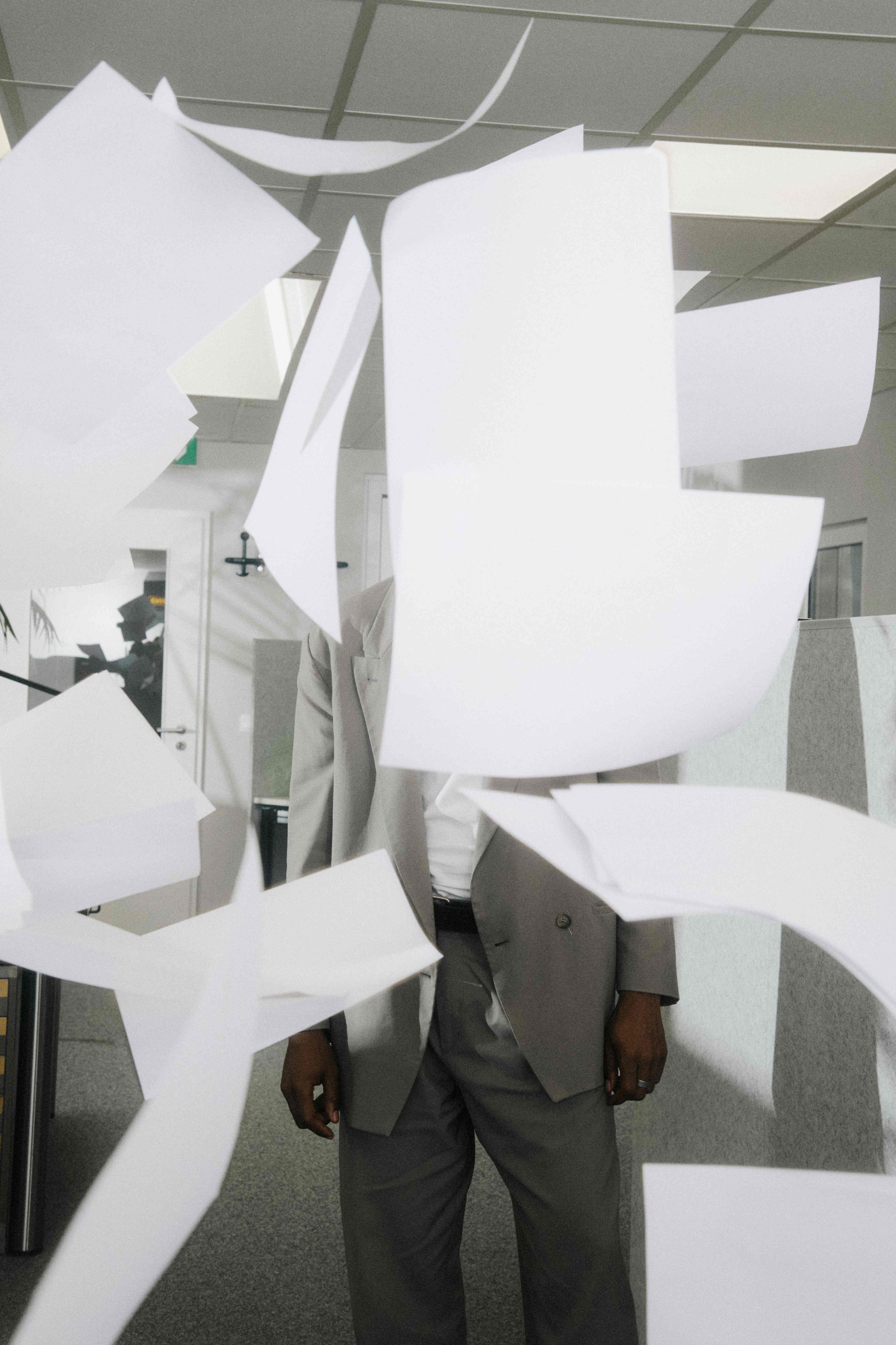 A person with their face fully obscured by flying sheets of paper — The Ad Spend brand image