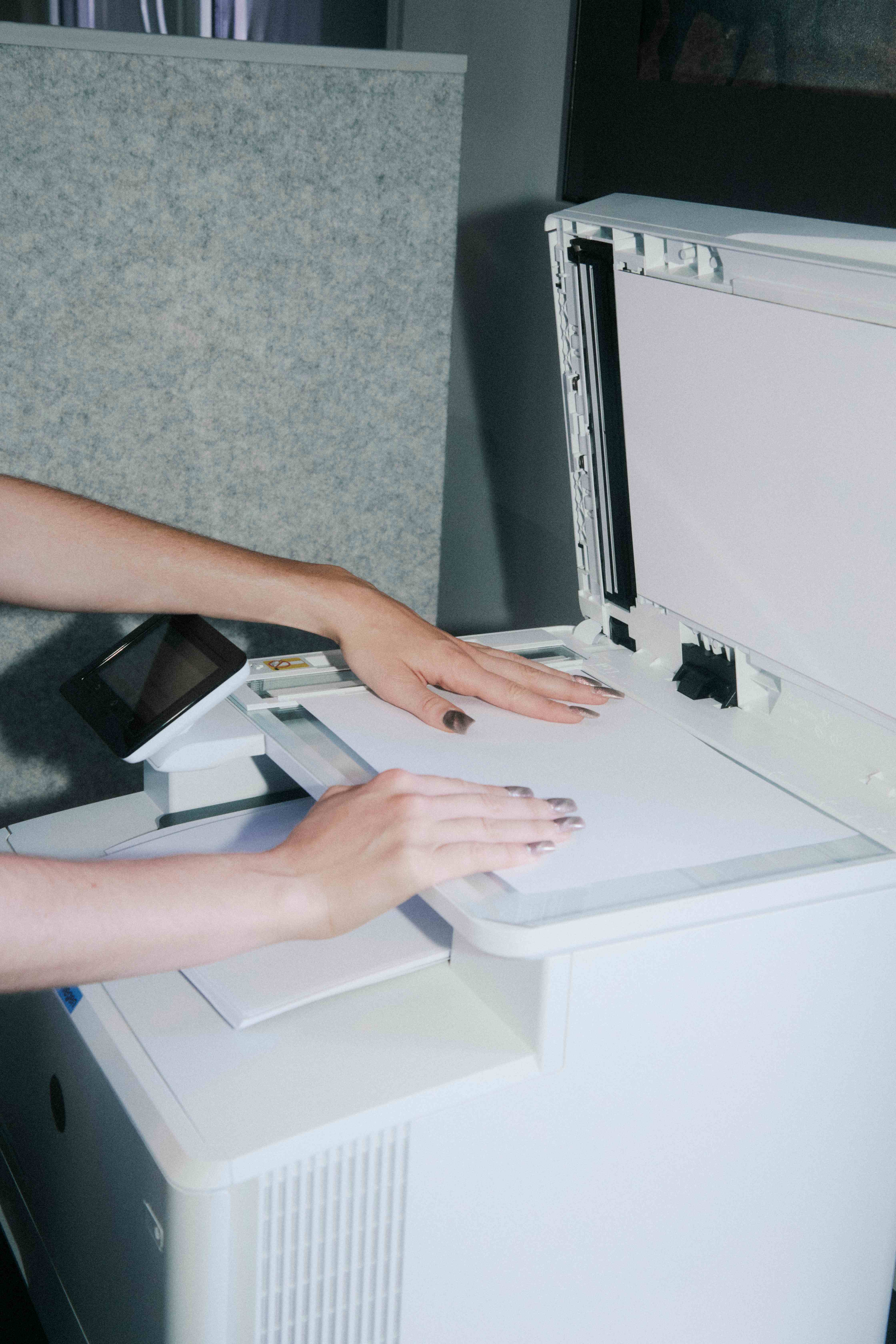 Hands placing a sheet on an open photocopier glass — The Ad Spend brand image