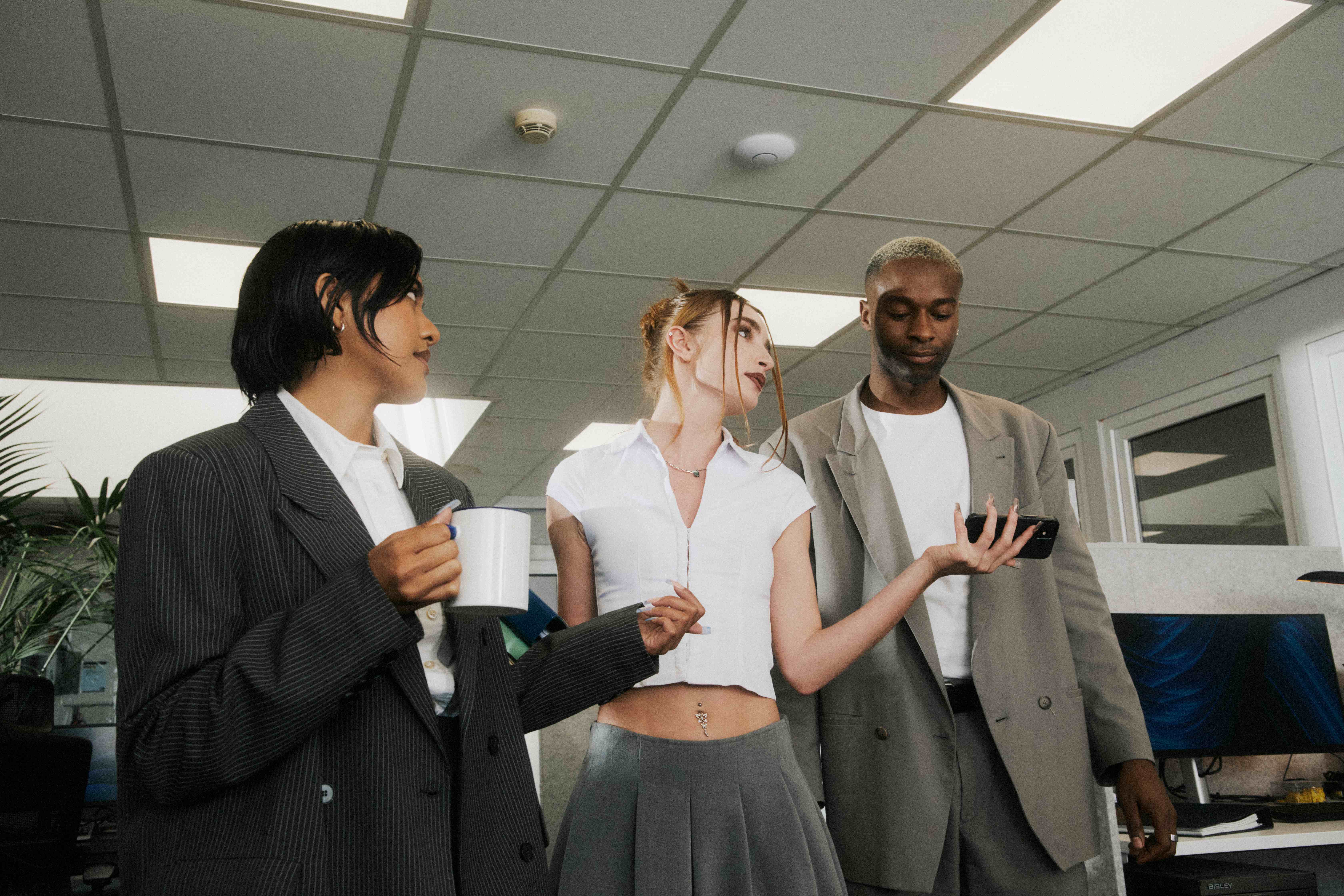 Three colleagues in discussion as one shares a phone screen with the group — The Ad Spend brand image