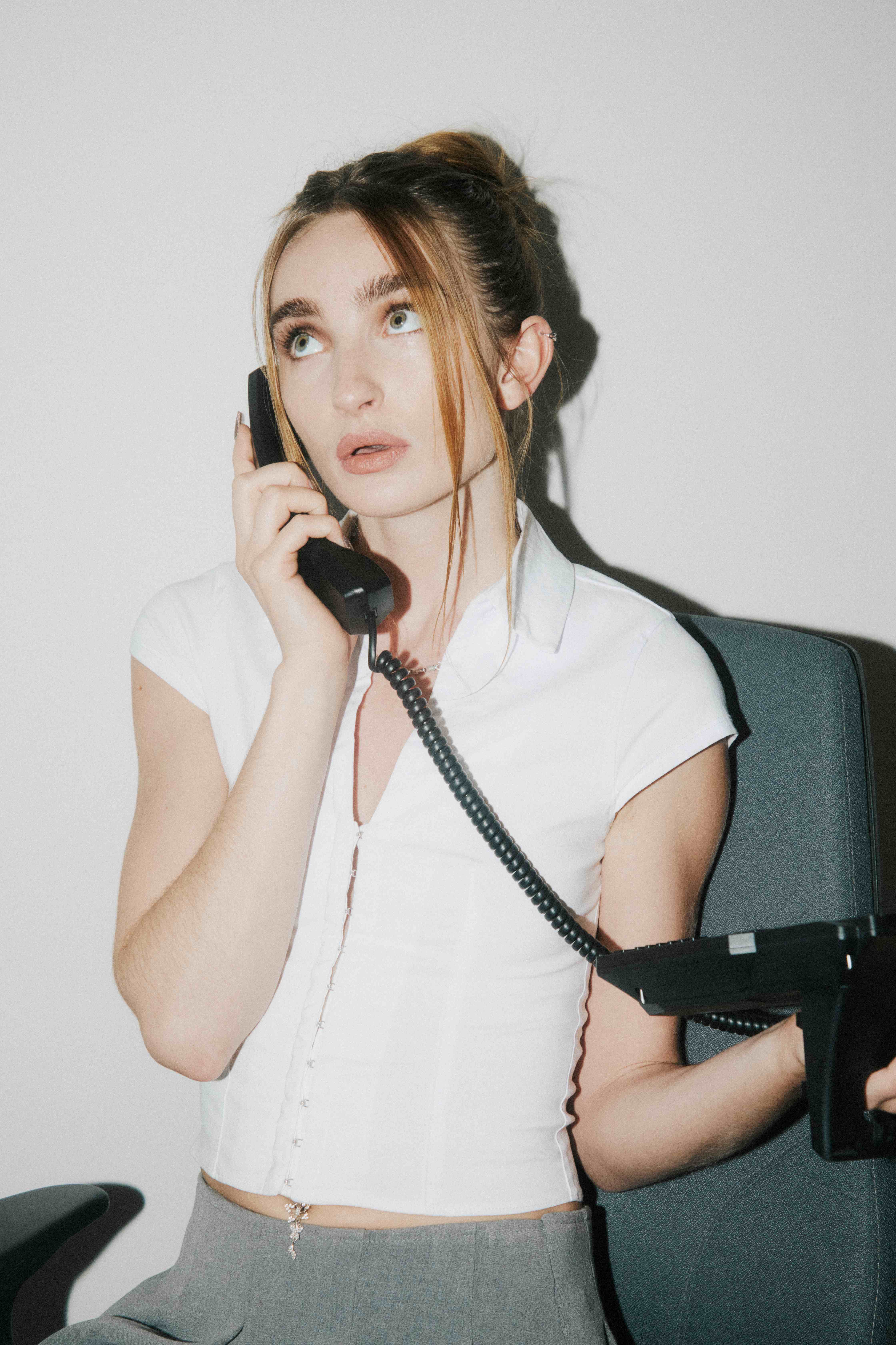 Woman on a corded desk phone looking up, holding the phone base — The Ad Spend brand image